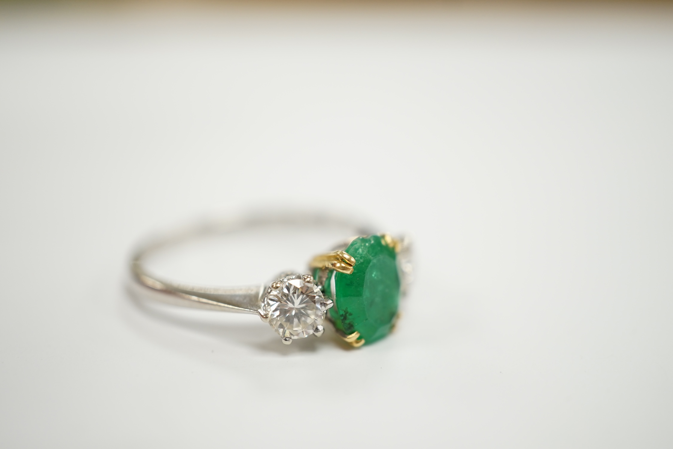 A 1970's 18ct white gold, single stone oval cut emerald and two stone diamond set ring, size P/Q, gross weight 3.2 grams.